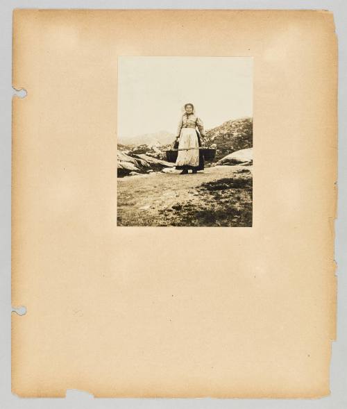 [A woman wears a hoop and pails with rocky hills behind her] Page 42 of Newfoundland from Collection of Canadian albums compiled by Edith S. Watson
