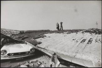 Three people stand on the flattened roof in the days after the mass destruction caused by the Friuli earthquake, 1976
