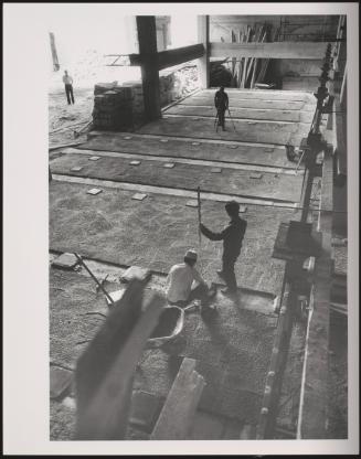 Seen from above, three construction workers laying down paving stones and cement