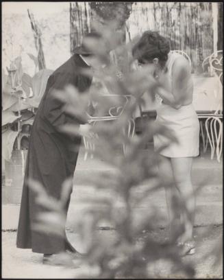 A priest and young women partially obscured by foliage