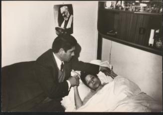 A man looks after an invalid woman lying in bed