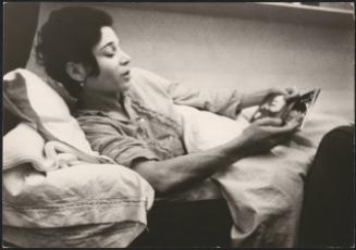 A woman looking at a booklet of religious cards lying in a bed