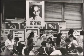 Children and mothers walking past a wall covered in communist posters including a poster of Vietnamese leader Ho Ci Min