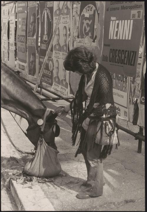 Portrait of a woman and a horse, behind them political posters line the sides of the street