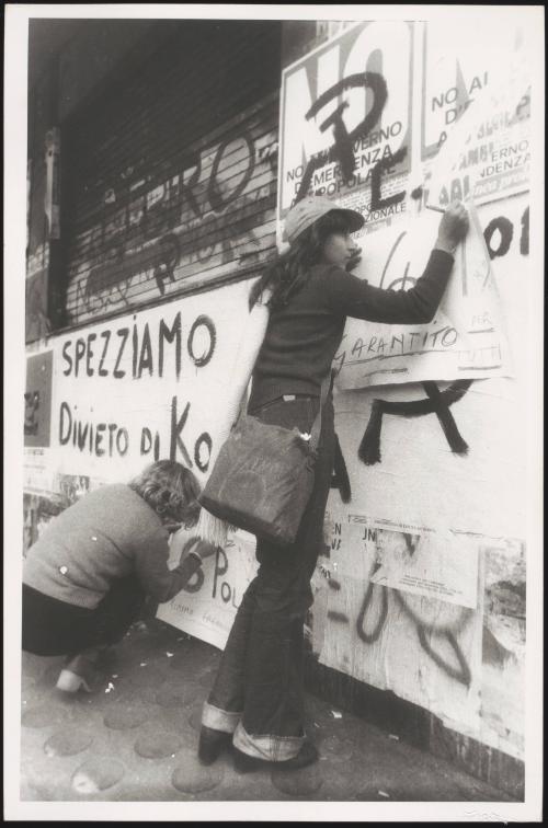 Two women pasting up communist posters on a wall