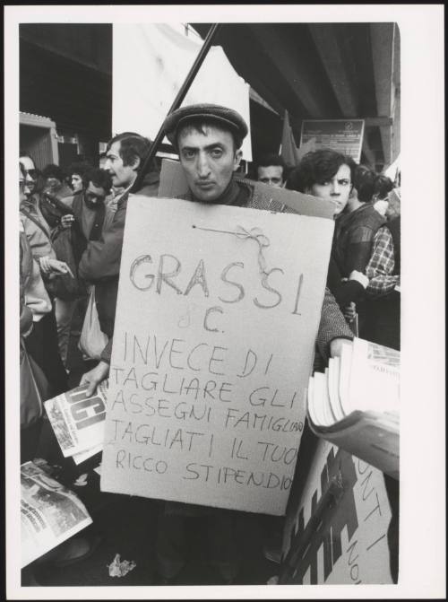 A man hands out protest papers and holds a placard with a message against cutting child benefits



