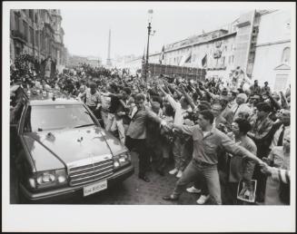 A large crowd gather on the streets to watch a car lead a Neo Fascist funeral procession 