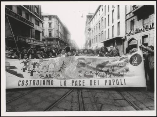 Milan 1982. A crowd of protesters march behind a large banner that reads 'costruiamo la pace dei popoli' down a street at a communist  peace march 