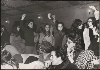 Women march through a crowded room, during a feminist protest in Rome, 1971