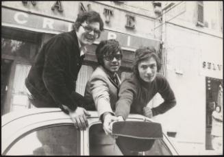 Three young freshman sit on top of a car