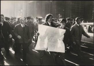 Men in military uniform march down the street at an anti school reform protest