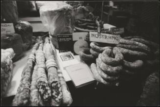 Bookshop table bearing books and cured meats, next to which a sign says 'NOSTRANO', meaning 'homegrown'