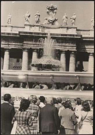 Tourists wait for a bus to pass before approaching a fountain