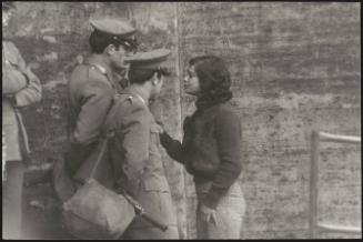 A young lady talks closely to three uniformed soldiers on a street