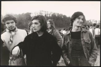 Three young men and women surrounded by crowds in a field