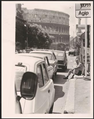 A man sits on the pavement near the colosseum in Rome