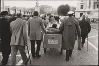 Men who were injured in the Great War march with walking sticks down the street with a motorized wheelchair as part of a protest for the disabled