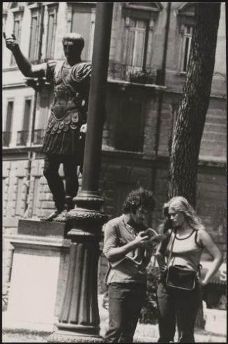 An Italian 'Pappagalli' man helps a female tourists consult a guide underneath a statue of Julius Caesar, Rome