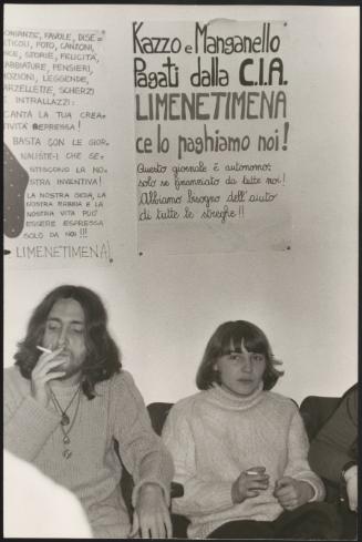 A young woman and man smoke together under posters for feminist newspaper 'Limenetimena'