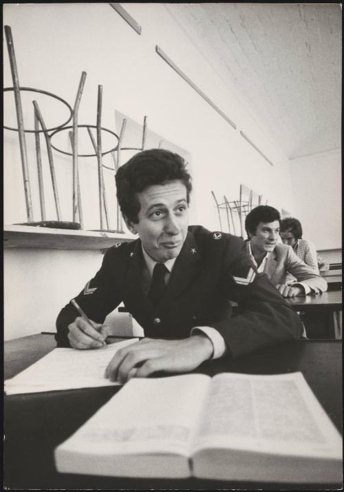 A university classroom, a working student in the uniform of an non-commissioned Airforce officer is taking notes during the lesson