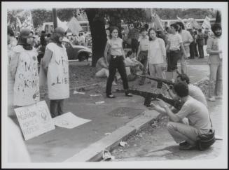 Two men aim their wooden rifles at two blindfolded women in a protest against Iranian leader Khomeini 