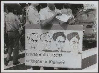 A young man wears a protest placard around his neck with cartoons of Iranian leader Khomeini