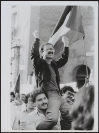Young men in a protest march through Italian streets, raising up a friend onto their shoulders