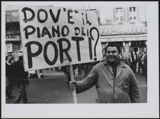 A disgruntled port worker holding a banner reading 'Where is the plan for the Ports?' at a protest of the port workers of Livorno