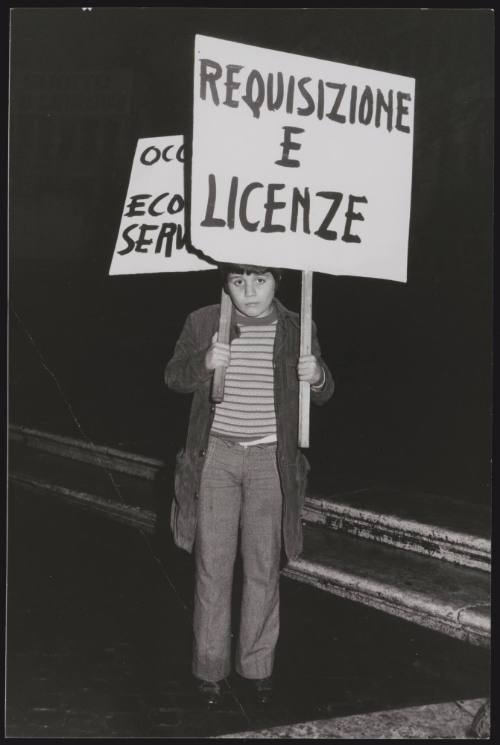A young boy holds a protest placard that reads "Requisizione e Licenze"