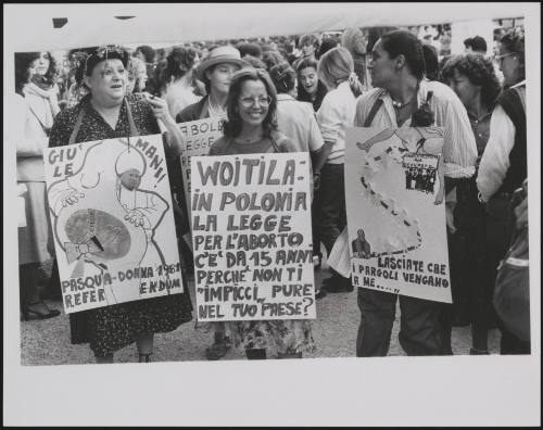 Three feminists wearing placards denouncing the law against abortion and criticising Pope Wojtyła about Poland's abortion law compared to Italy's