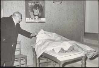 A man looks at a victim laid under a sheet in the aftermath of an earthquake, 1971