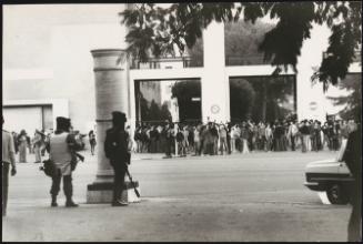 Riot police on stand by as protesters gather outside a building.