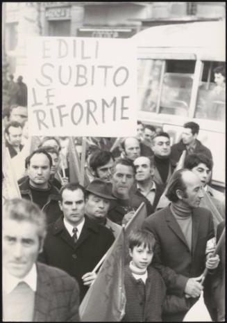 Construction workers demonstrate in the streets. A placard reads:
'Edili subito le riforme'
'Construction suffers from reform'