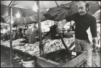 A man holds an eel at a fish stall on market day
