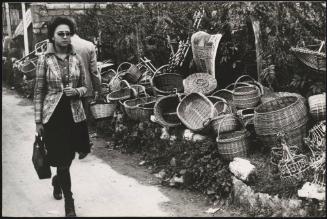 A womanwalks by wicker baskets for sale, lining the road on market day