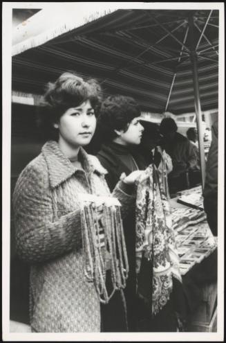 Two young women sell strings of beads and scarves at the market
