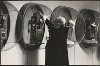 A priest feeds coins into a pay box telephone at an airport