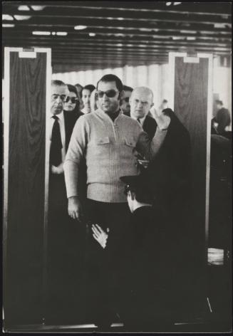 A man in sunglasses is patted down as he walks through airport security 