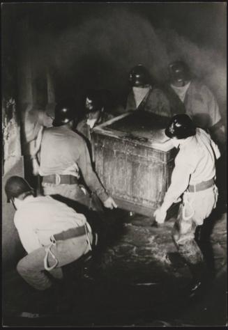 A team of policemen with their faces covered carry a heavy chest during the Belice earthquake rescue, Sicily 1968