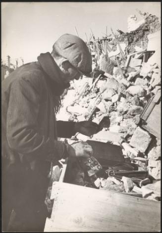 A survivor of the Belice earthquake looks through the rubble of destroyed homes, Sicily 1968