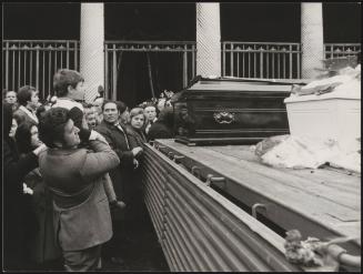 A young boy is picked up by his father in a crowd to pay respects to a coffin in the aftermath of the Belice earthquake, 1968