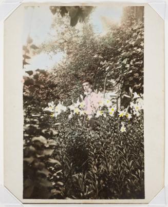 A young man wearing a pink shirt among lilies in a garden