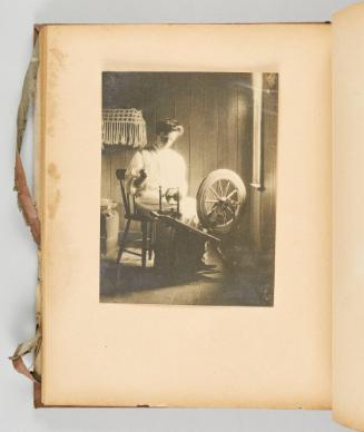 [A woman works at her wheel in soft daylight with intricate textile work on the wall.] [Page 57 of Quebec I; from collection of Canadian albums compiled by Edith S. Watson, 1890s-1930s]