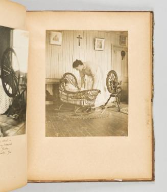 [Woman tends to her baby in a wicker cradle, with her spinning wheel nearby] [Page 42 of Quebec I; from collection of Canadian albums compiled by Edith S. Watson, 1890s-1930s.]