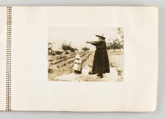 [Woman letting grain sift through her fingers, with child beneath her, page 19 of The Doukhobors I album]
