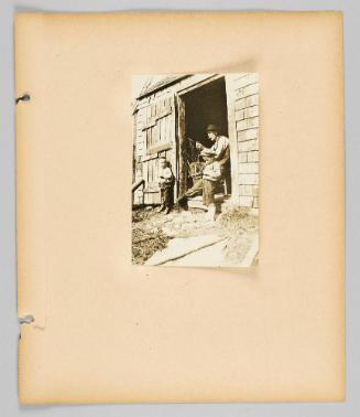 [Two boys stand outside of barn with elderly man, page 63 of Children album]
