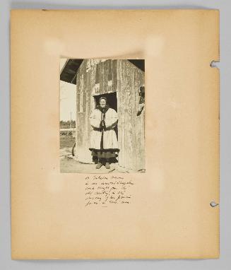 A Galician woman in an inverted sheepskin coat brought from the old country, in the doorway of her prairie farm in Gonor, Manitoba [Page 8 of New Canadians album]
