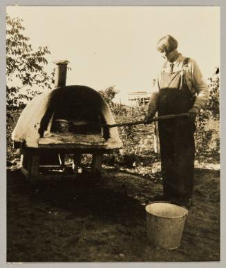 A "farmerette" of the Canadian prairie tendig the big loaves of bread a-baking in the out-of-door oven In Gonor, Man.
