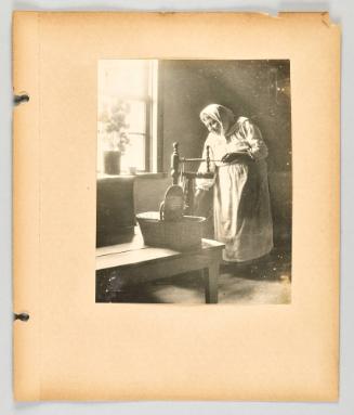 [Woman working at her spinning wheel beside window with flowers displayed], page 31 of The Doukhobors II album]