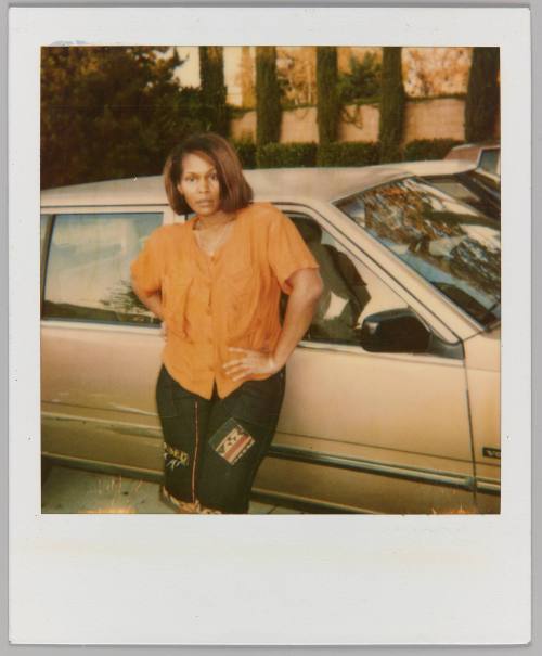 [Woman in orange blouse posing in front of tan volvo]
